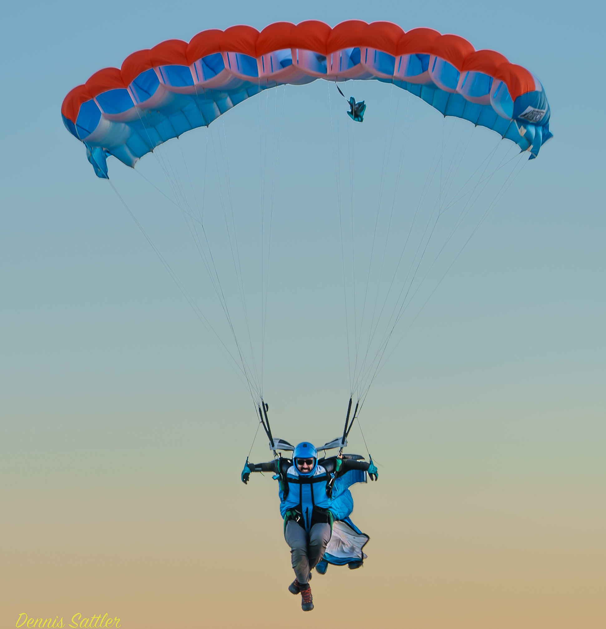 wingsuit skydiver coming in for landing under a parachute 