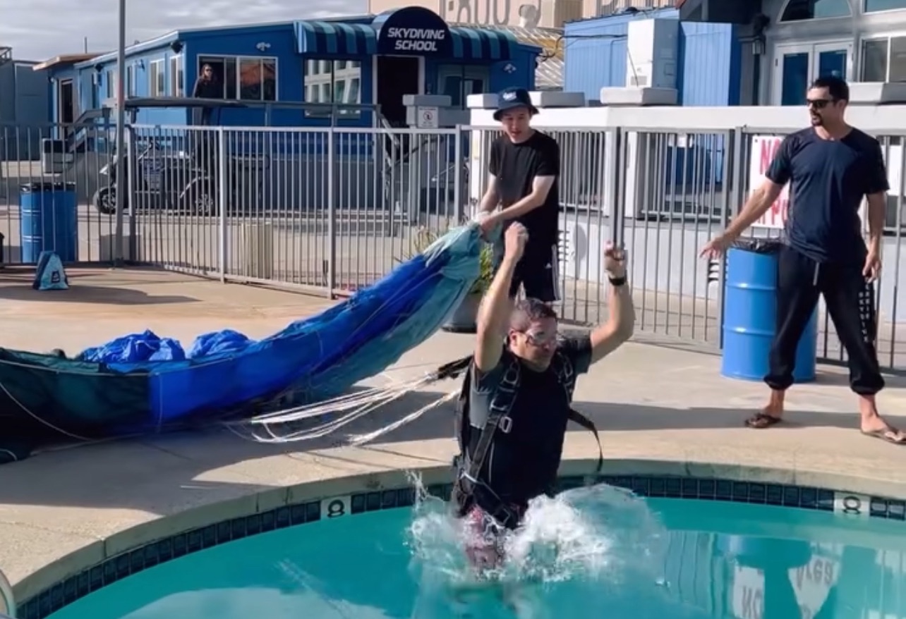 skydiver practices water training by jumping into a pool with a parachute